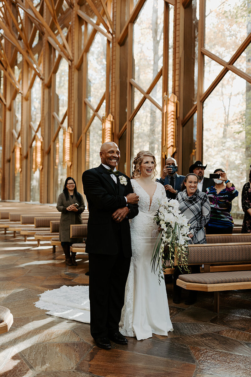 Bride being given away by her best friend's dad during the ceremony at Anthony Chapel located at Garvan Gardens in Hot Springs, Arkansas. One of three glass chapels in Arkansas by E. Fay Jones.