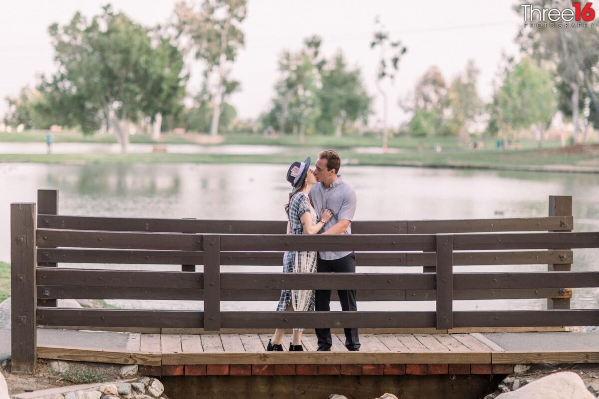 Married to be couple share a kiss on a wooden bridge at Tri-City Park