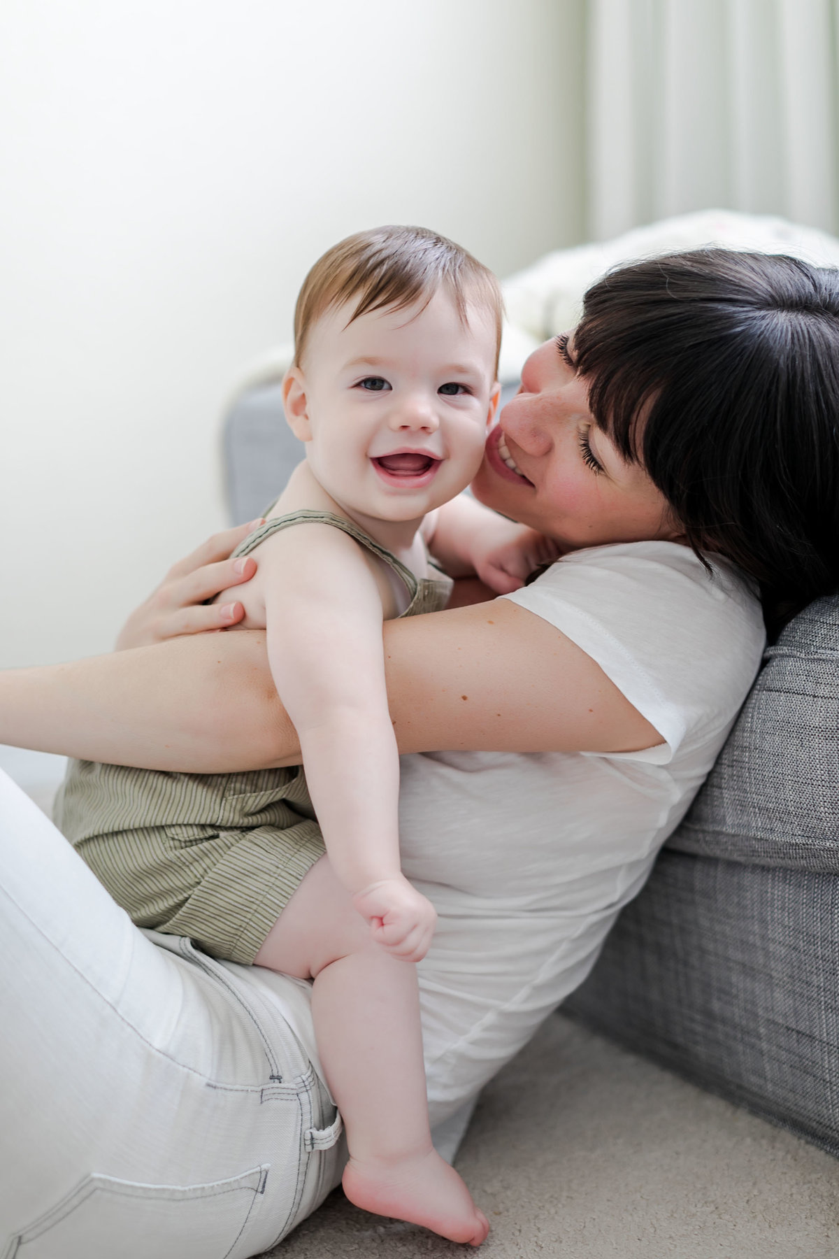 A laughing toddler snuggles into his mother's arms during a light-filled lifestyle session at home, captured by Brooke Tucker photography in Virginia Beach