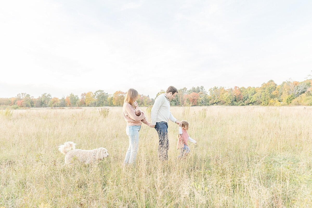 family walks through field in Natick Massachusetts during outdoor newborn photo session with Sara Sniderman Photography