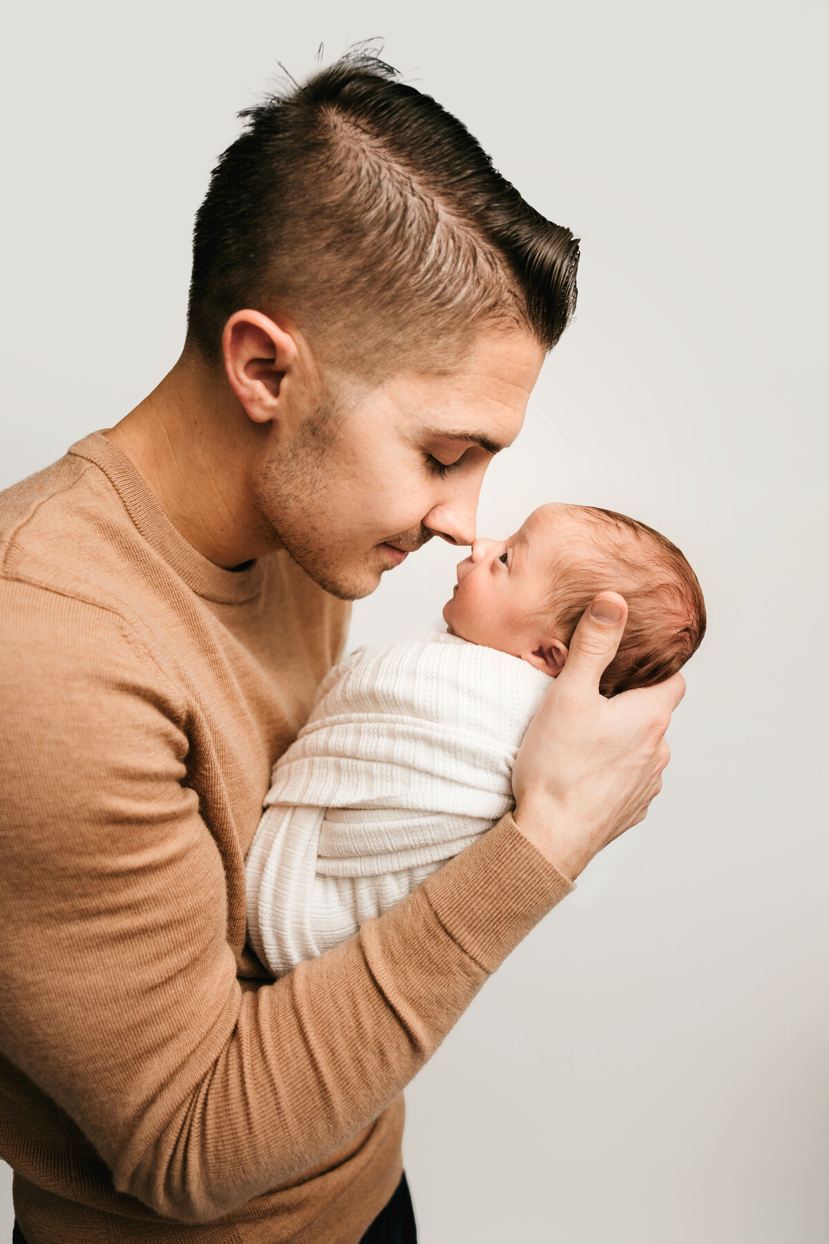 A dad holds his newborn son and softly touches noses.