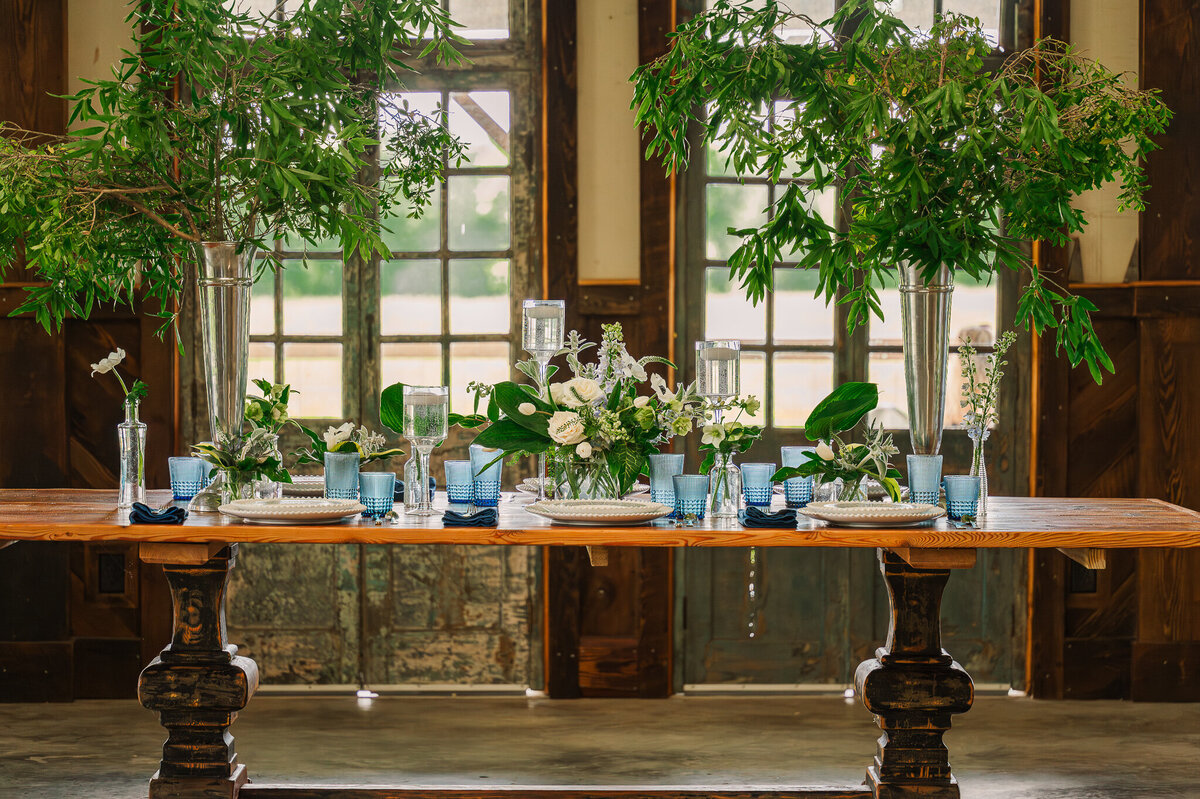 A rustic tablescape full of greenery and blue antique glasses at Highrock Farms by Raleigh wedding photographer JoLynn Photography