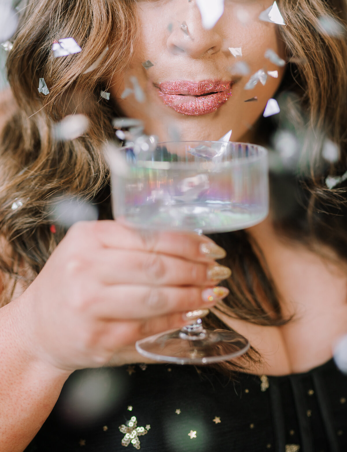 Close-up beauty shot of a woman with glitter lips holding a champagne glass surrounded by flying confetti — shot by Dani Lacey in Greenville SC for a glam, festive branding look.