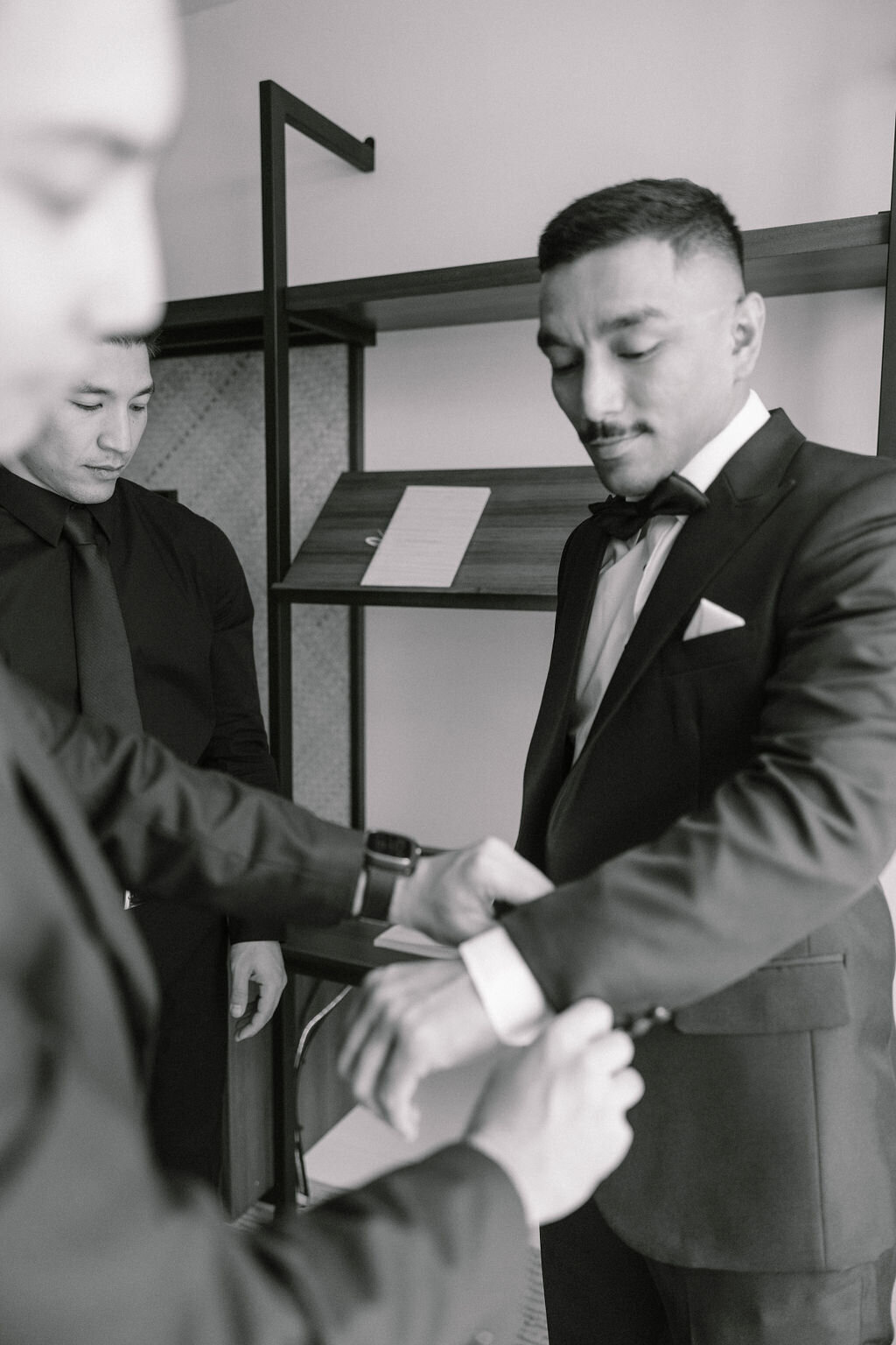 groomsmen helping groom with his tuxedo cuffs in hotel room at laylow waikiki