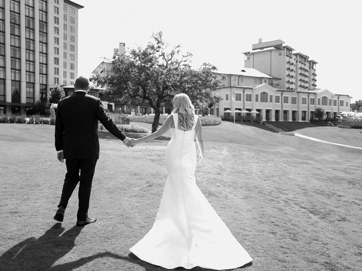 Black and white image of a bride and groom walking together back towards the hotel