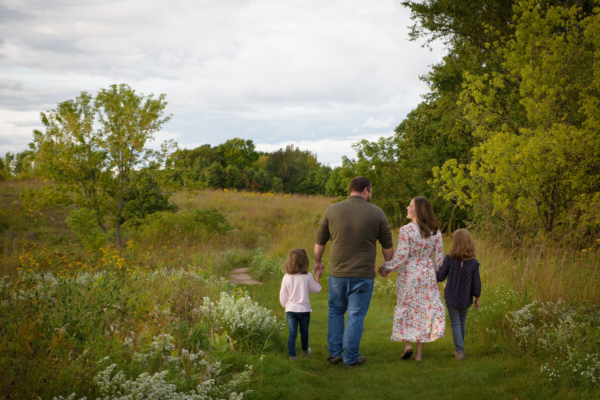 Portrait of a family of four walking away from the camera in a long grassy field at Fonferek Glen County Park near Green Bay, Wisconsin.