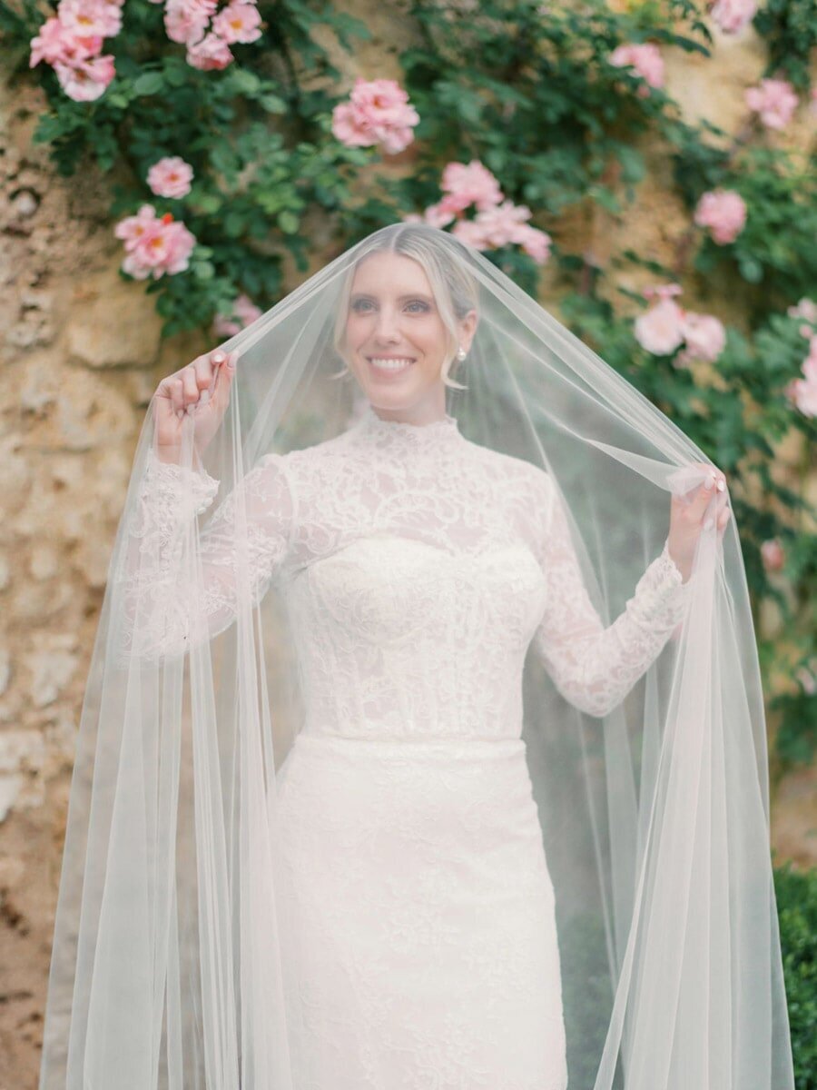 Outdoor bridal portrait of bride under veil, in front of roses and a wall at Borgo Santo Pietro in Tuscany