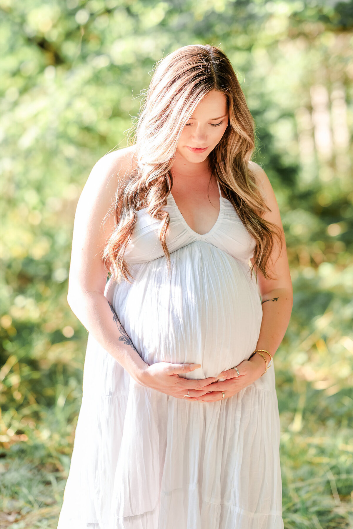 A pregnant woman cradles her belly during her Chesapeake maternity photography session. She wears a simple white dress.