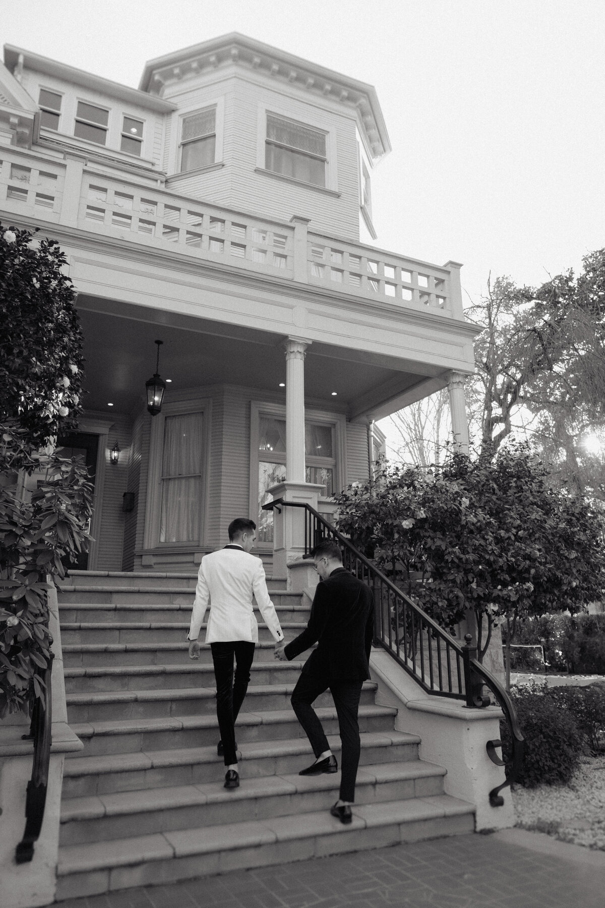 Two grooms walk up the steps of an elegant historic venue, captured in a refined, editorial wedding photo that highlights love and sophistication.
