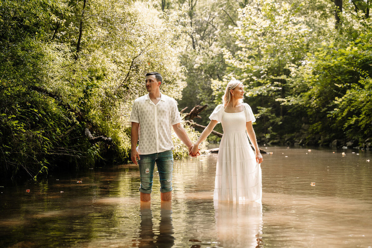 Couple standing in a creek, holding hands surrounded by lush greenery