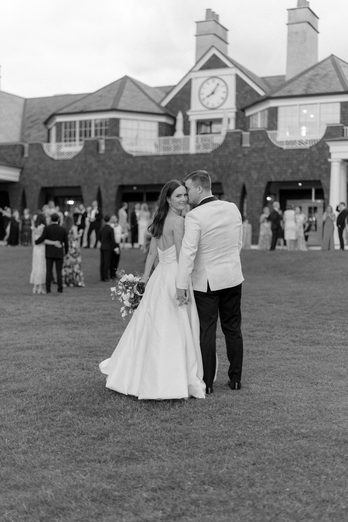 Bride looks back at camera with groom kissing check. Cocktail hour wedding day portraits at the River Course Kiawah Island. Destination wedding photographer.