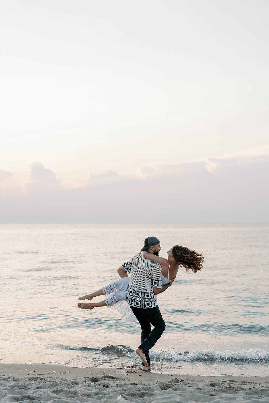 Romantic Lake Michigan engagement photo of groom lifting his fiancée in the water at New Buffalo Beach