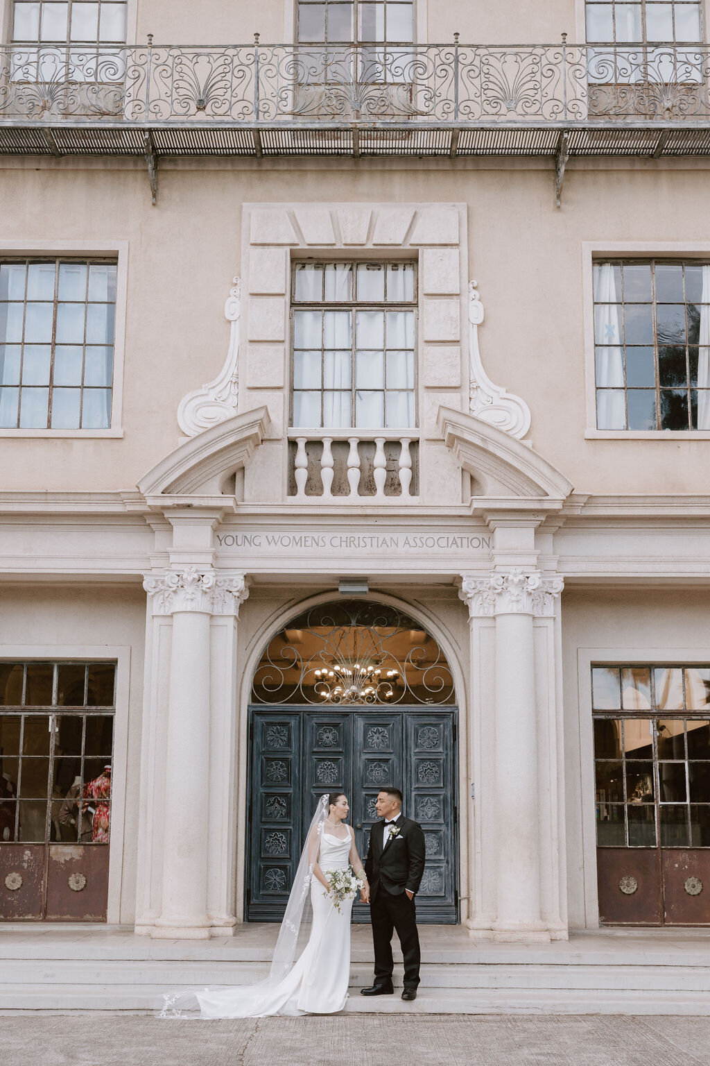 Bride and groom in front of the Cafe Julia Hawaii building with european architecture and a large black door