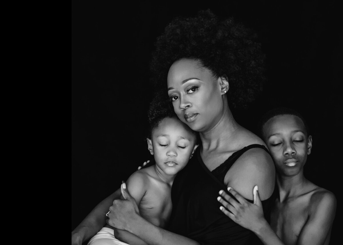 Black and white portrait of dark skinned woman with her two sons posed in front of a black backdrop