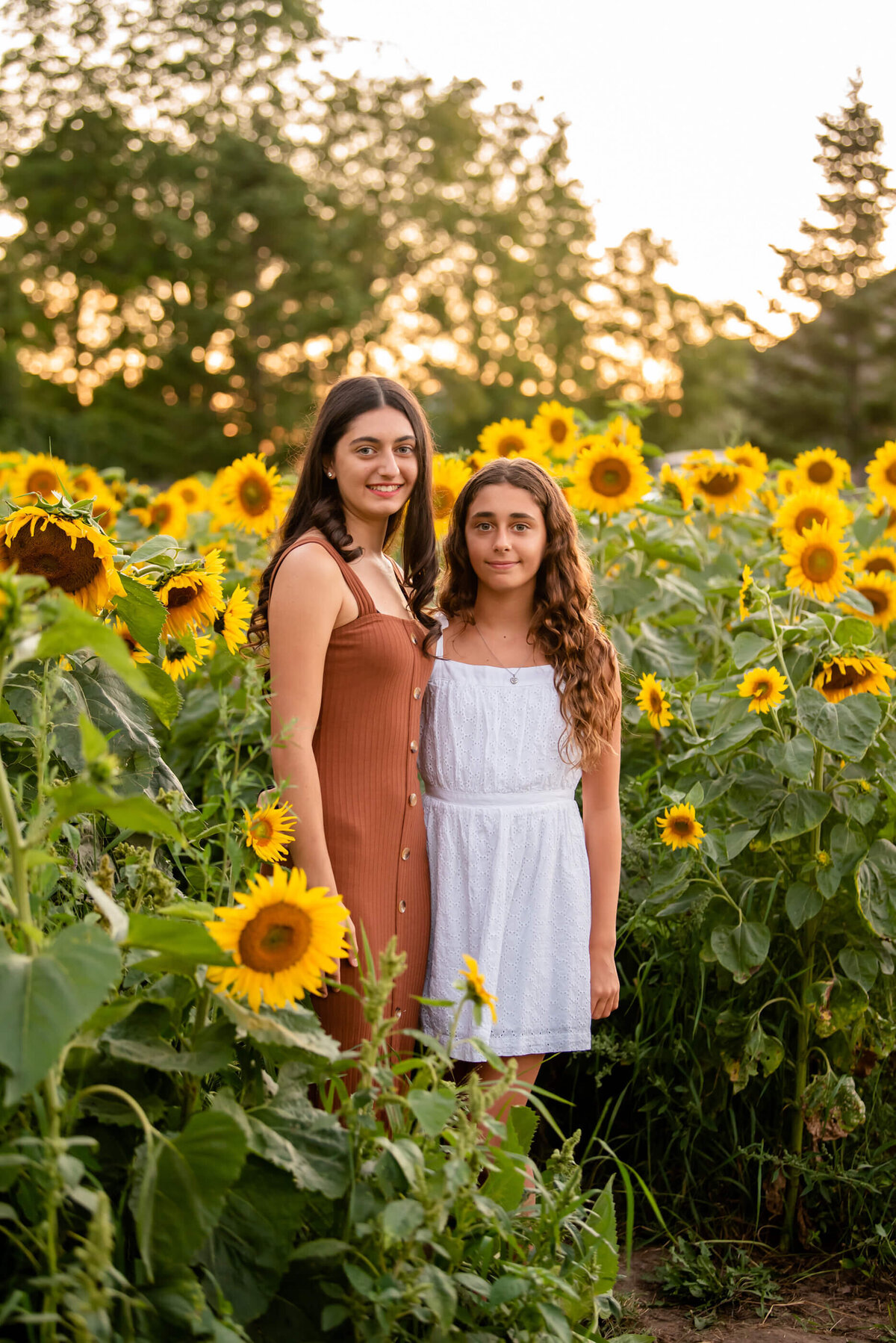 teenage sisters standing in a sunflower field for their family photography session