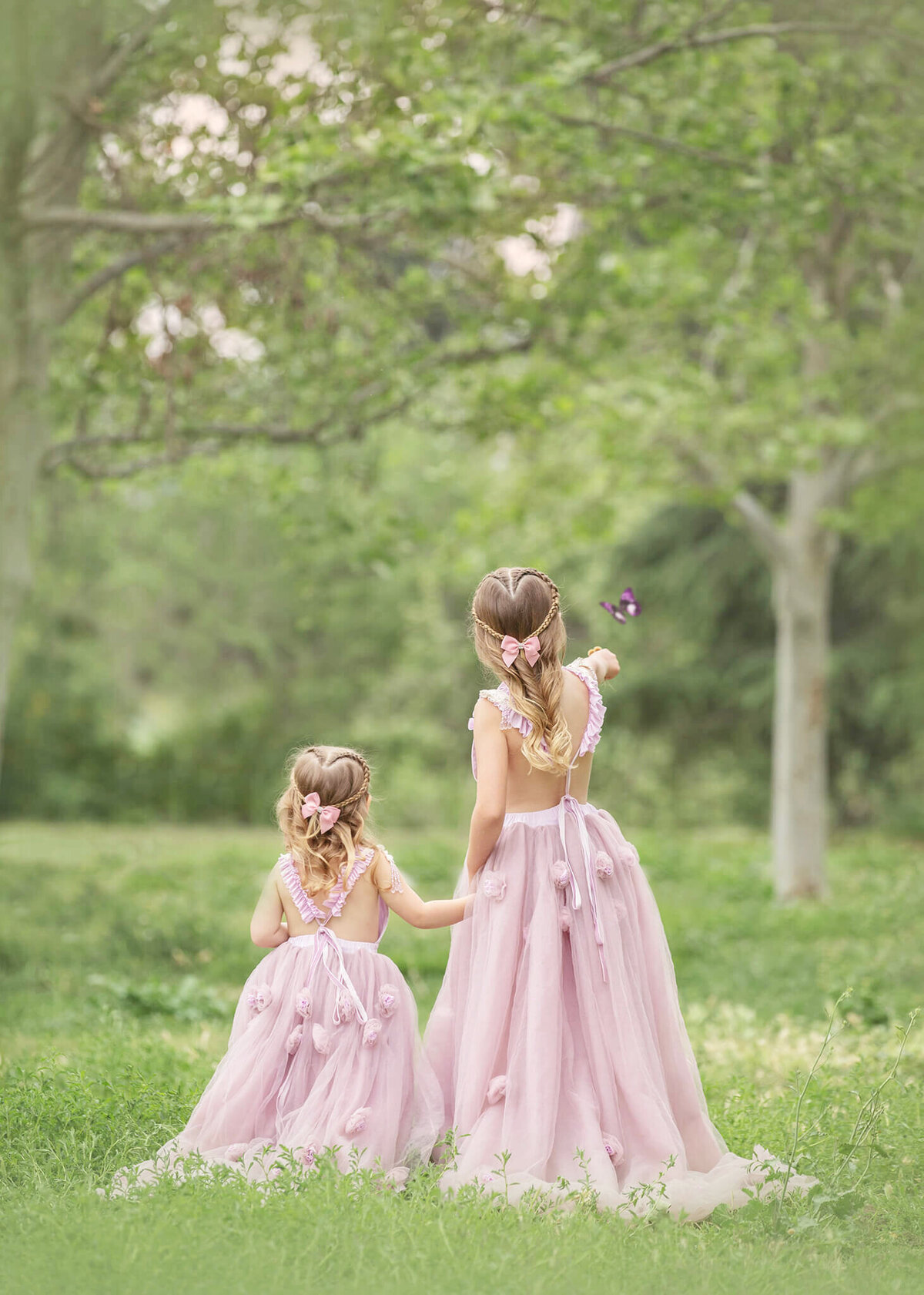 Sisters holding hands and facing away from camera in the green grass at Spring time