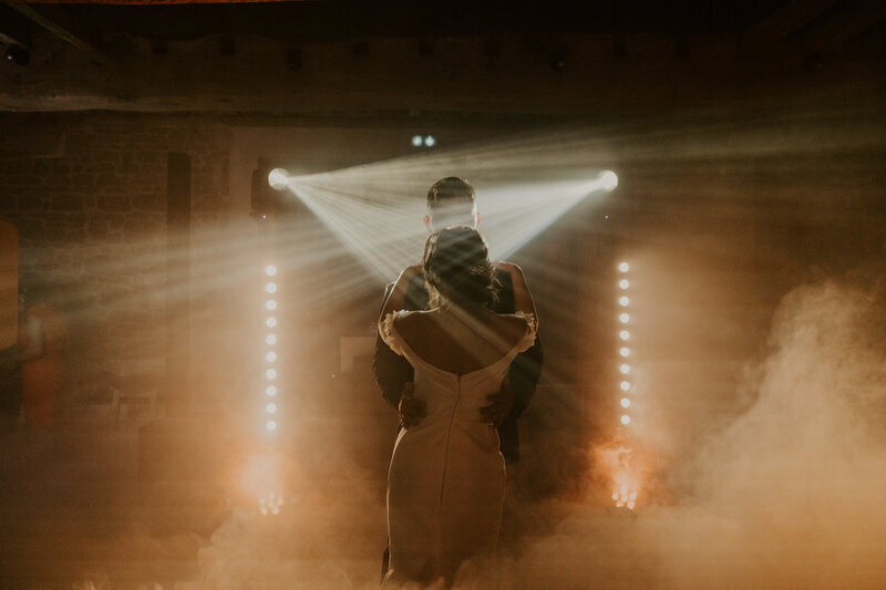 Couple de marié dansant, la femmed e dos, le mari caché derrière elle, entourés de fumée orangée et sous les projecteurs. Scène immortalisée par Laura Termeau photographie.