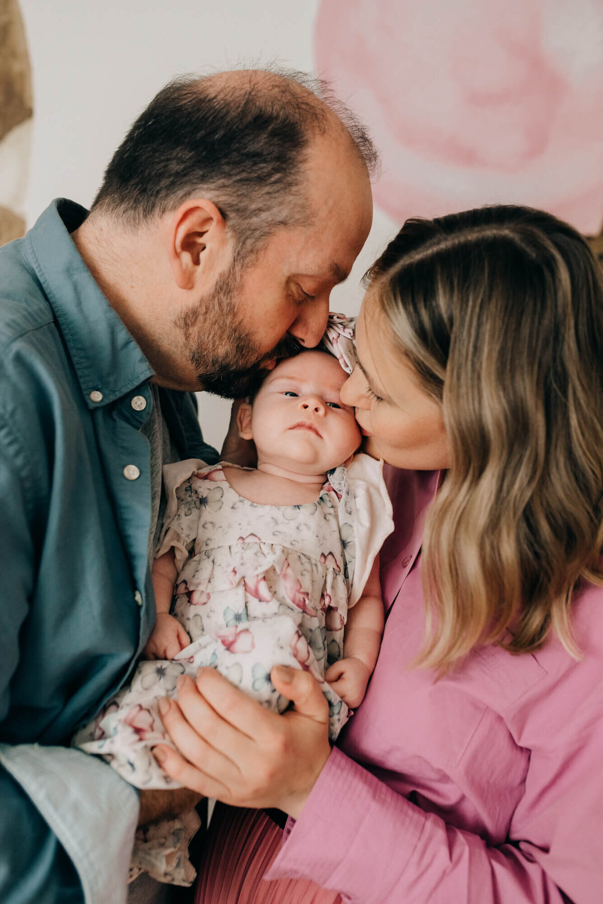 A mother and father give their newborn baby girl a kiss at the same time in her safari themed nursery