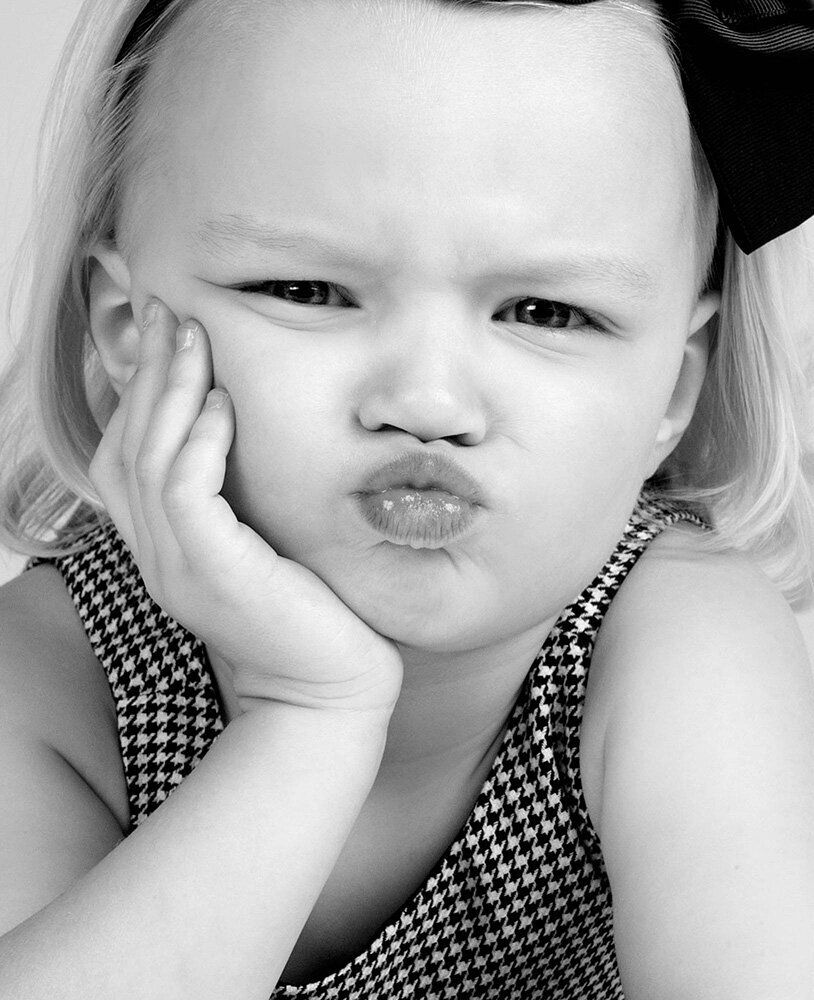 A cheerful little girl wearing a colorful bow on her head, smiling brightly at the camera.