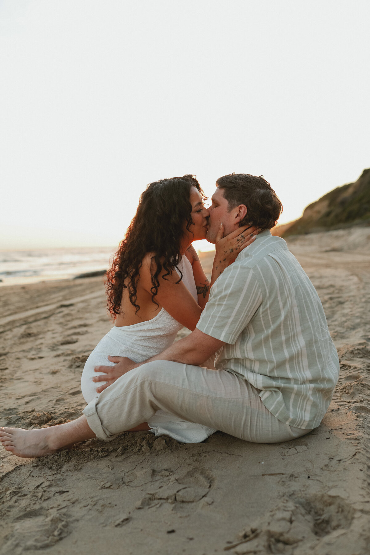 couole sitting on the beach kissing with bluffs in the back round