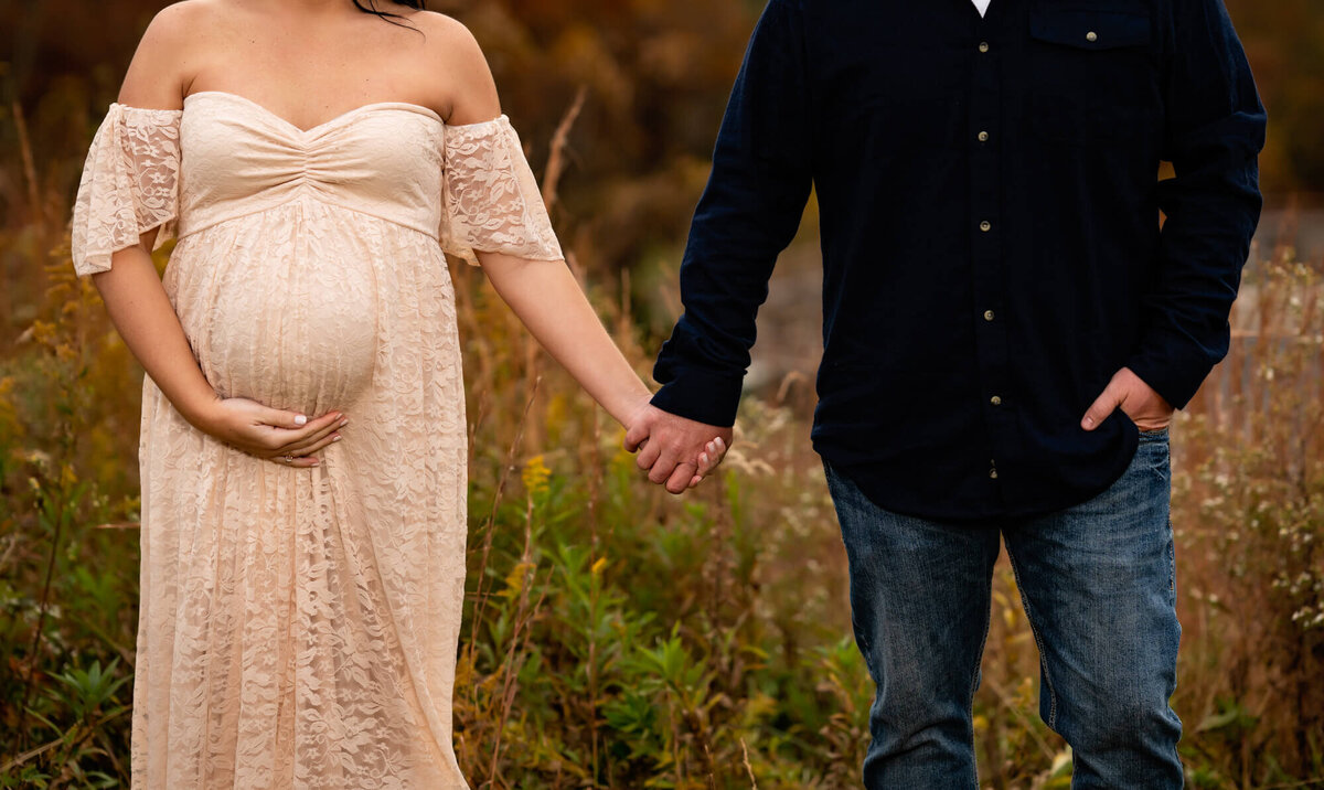 A detail portrait of an expecting couple holding hands and cradling the baby bump