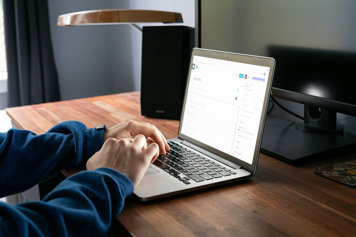Close-up shot of a white man in a blue shirt, working on a laptop at his desk.