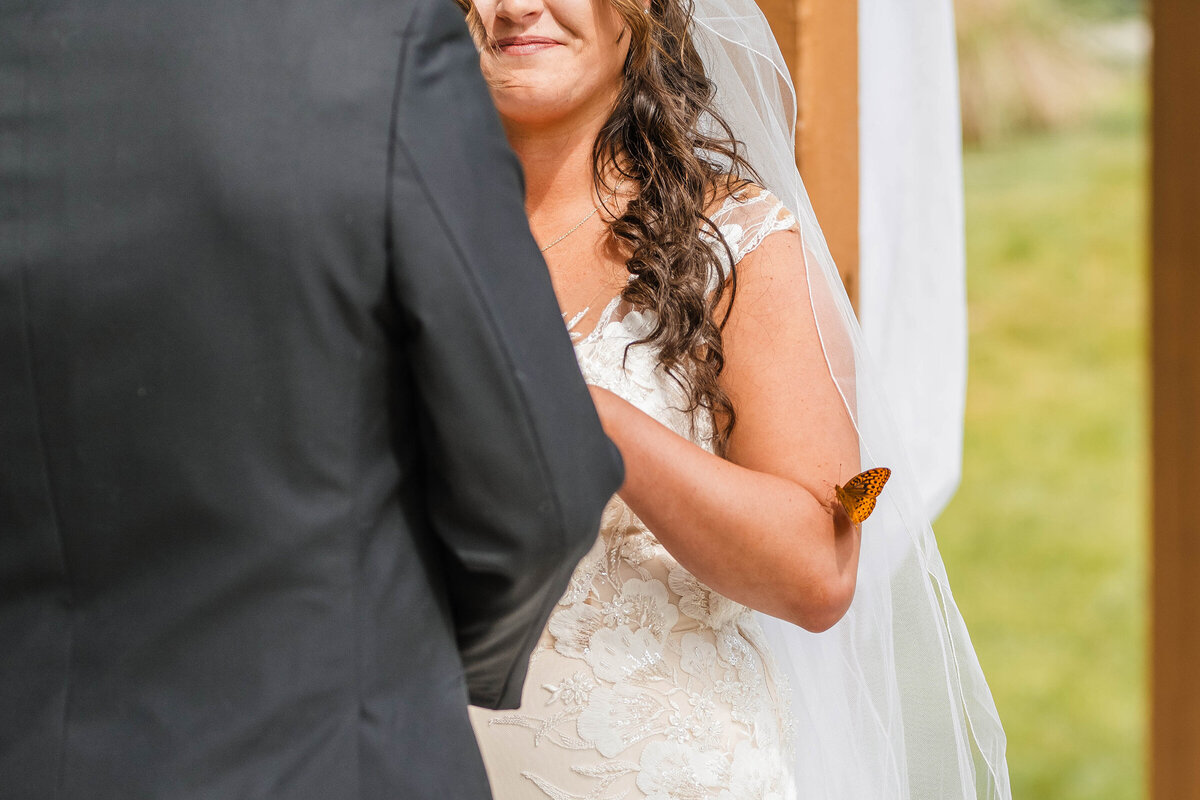 Butterfly lands gently on brides arm during wedding ceremony.
