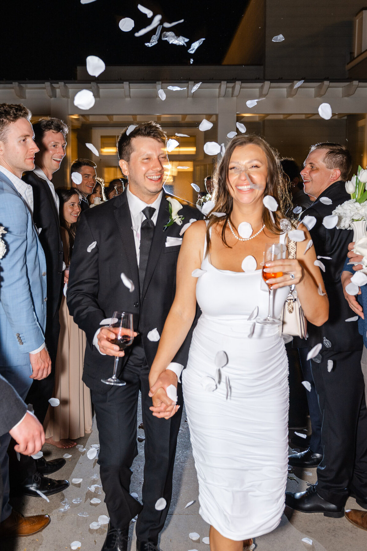 The bride and groom walk hand in hand through a tunnel of guests tossing flower petals during a magical wedding exit at Lido House in Newport Beach