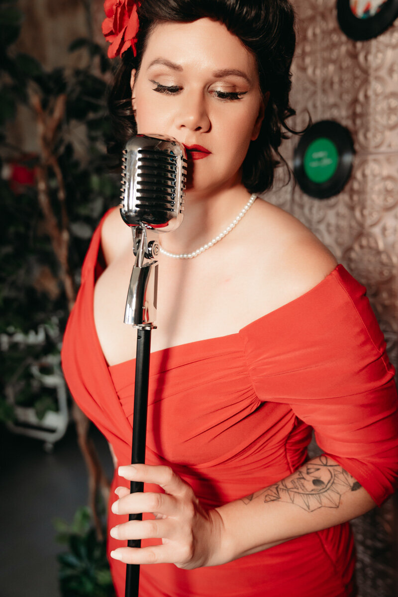Pinup woman in red dress with dark hair and red flower singing into a microphone