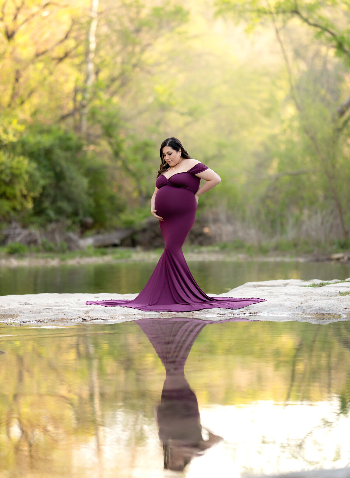 Mom-to-be in deep purple gown by the water with forest reflections in Georgetown, TX maternity session