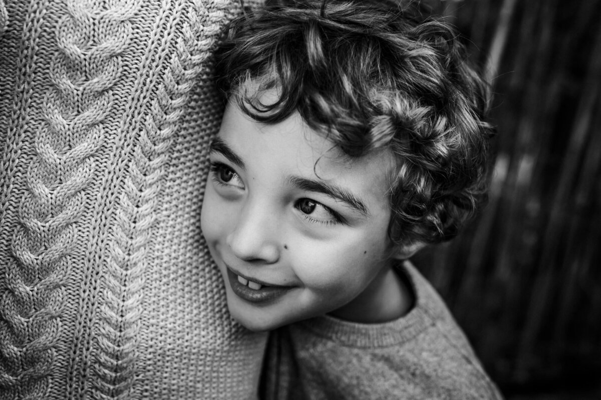 8-year-old boy smiling and looking away from camera as he leans on mom