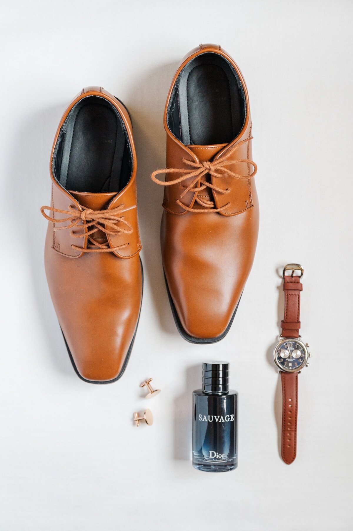 A flat lay of a groom's shoes, cologne, cufflinks, and watch. 