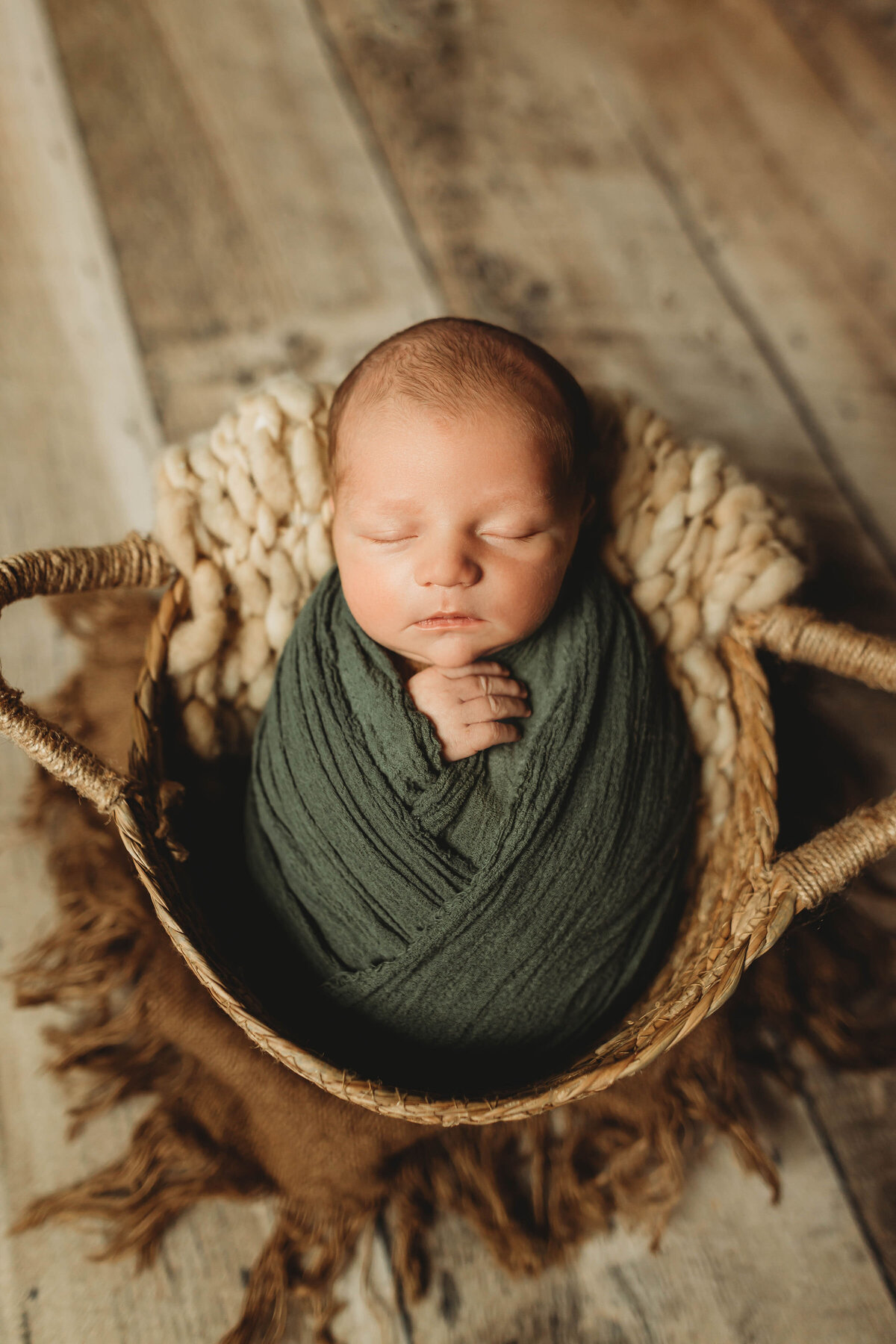 baby wrapped in green in a wooden basket.