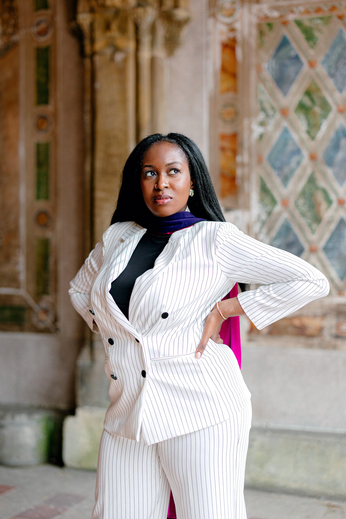Fordham Law graduate posing confidently in white suit and purple hood at Central Park.