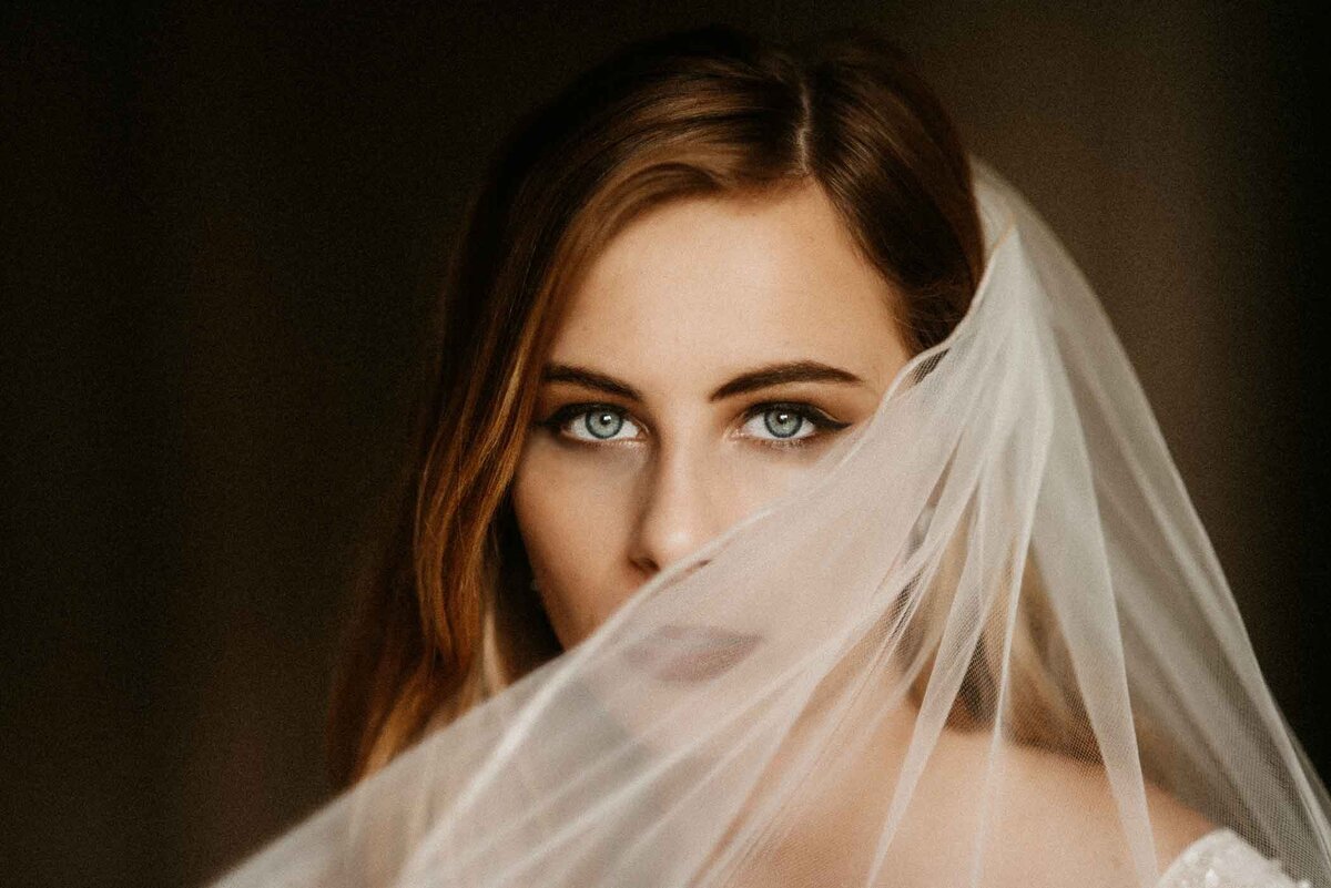 Bride-close-up-looking-at-camera-ice-blue-eyes-and-veil-covering-half-her-face-Missouri-fine-art-wedding-photographer