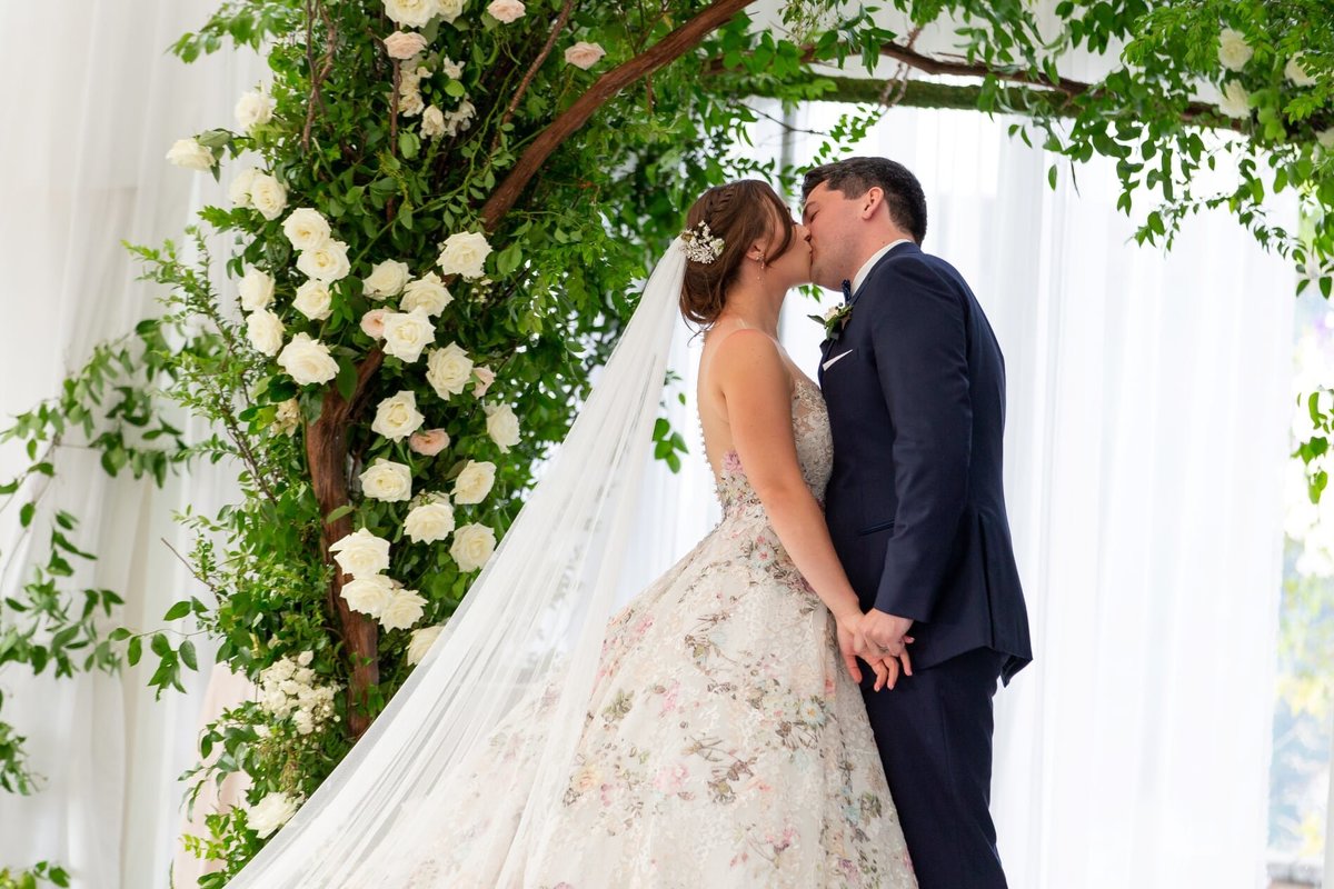 Wedding couple kissing under greenery wedding arch