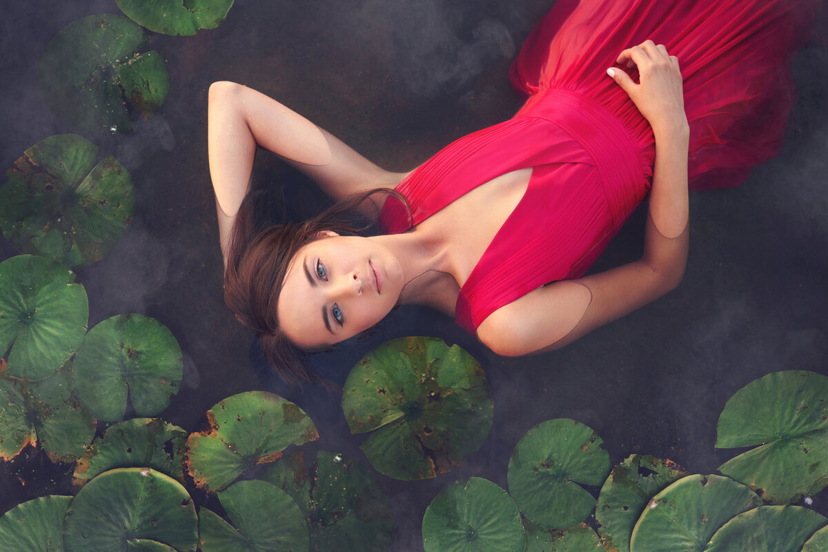 creative senior portrait lying in lillypad pond water