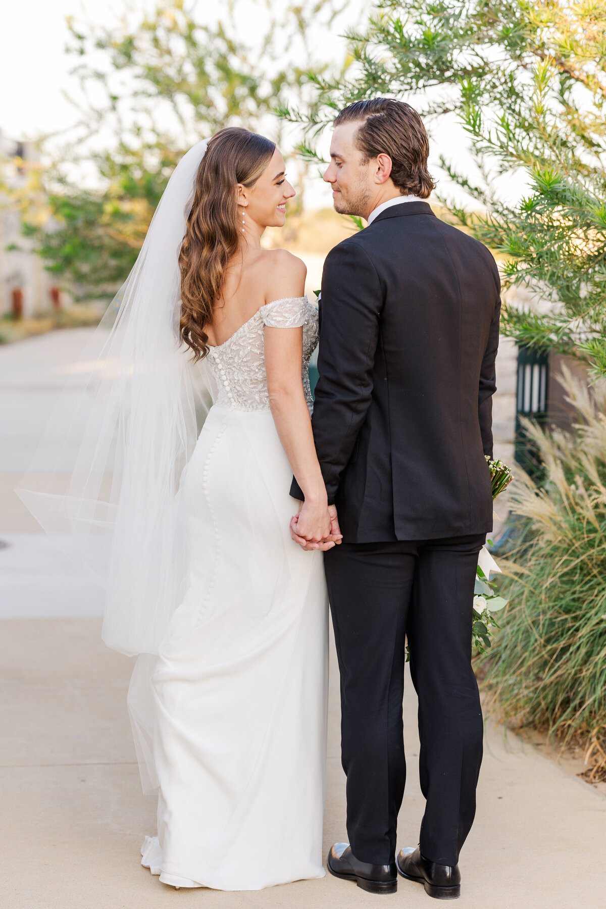 The bride and groom share a quiet moment hand in hand, walking through a serene outdoor path at their upscale wedding near Fort Worth, Texas.
