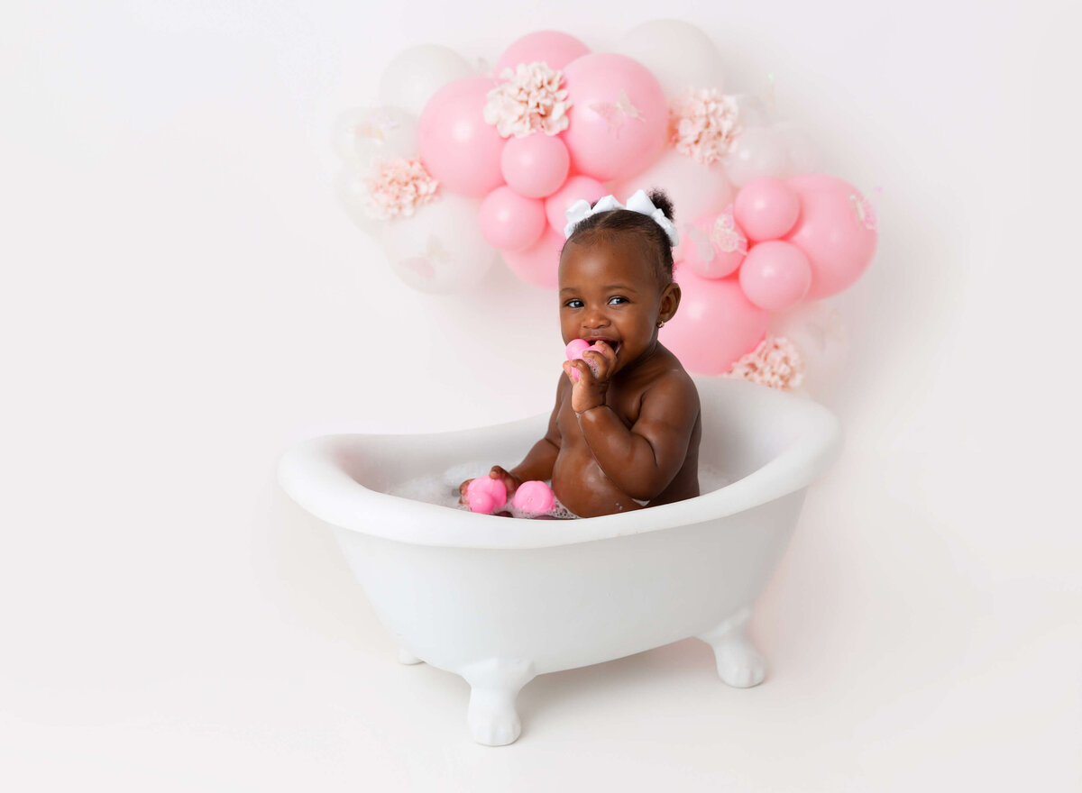 Baby girl sits in bubble bath white pink ballon garland cake smash