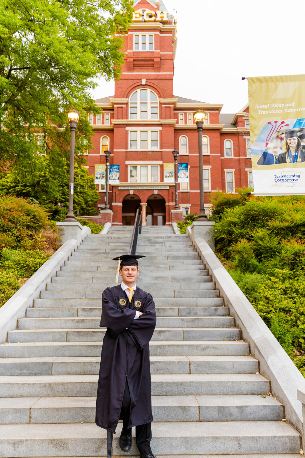 College graduate standing arm crossed wearing graduation cap and gown in front of the Georgia Tech campus tower stairs during senior portraits with Atlanta photographer Laure Photography