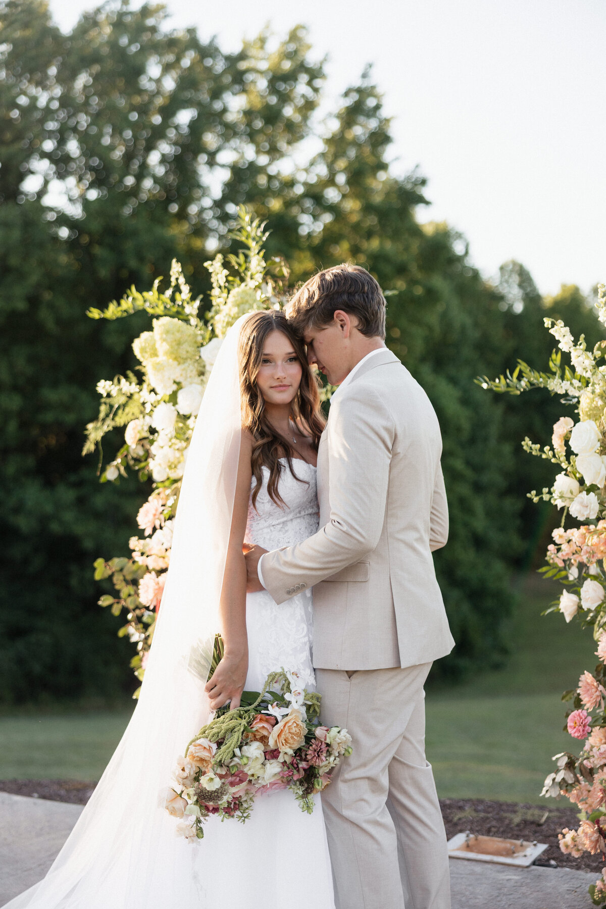 Groom laying his head on his bride on their wedding day as she looks beautiful in the susnet.
