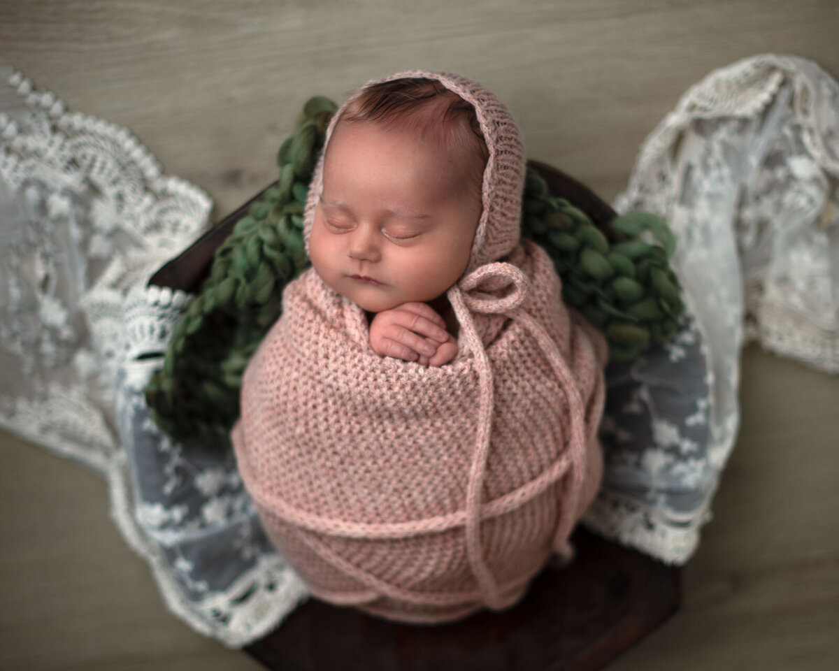 baby with pink wrap and bonnet in a bowl with green and lace blankets underneath by st. louis newborn photographer, sutherland photography