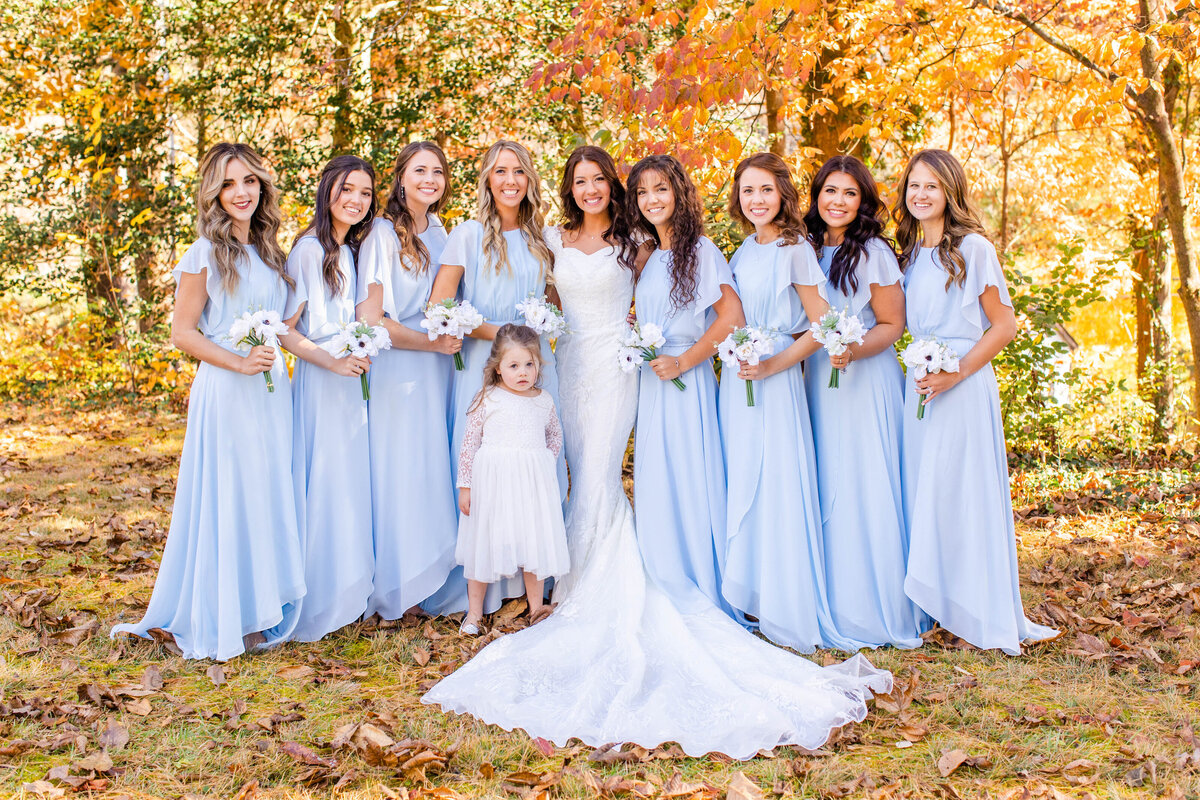 bridesmaids posing with flower girl in fall leaves