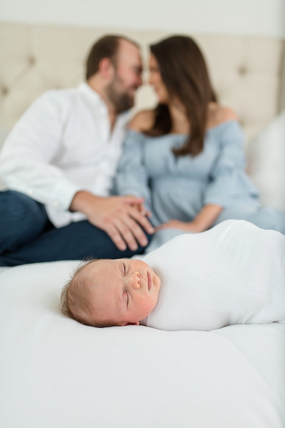 Baby boy on bed with parents kissing behind him