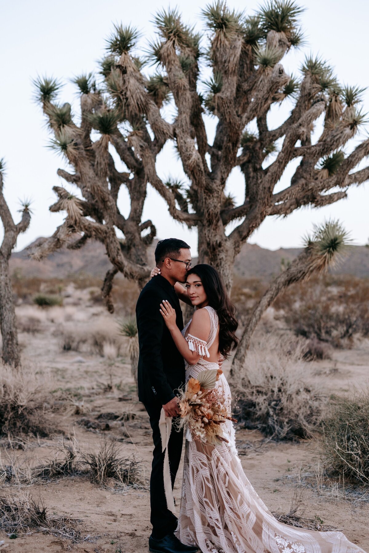Bride and groom posing in front of a large cactus.