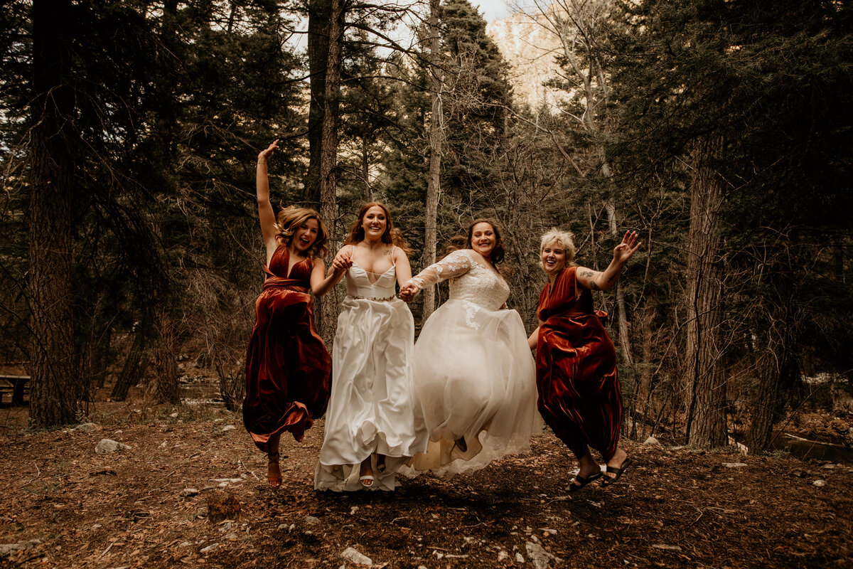 two brides and two maids of honor jumping in wedding clothes
