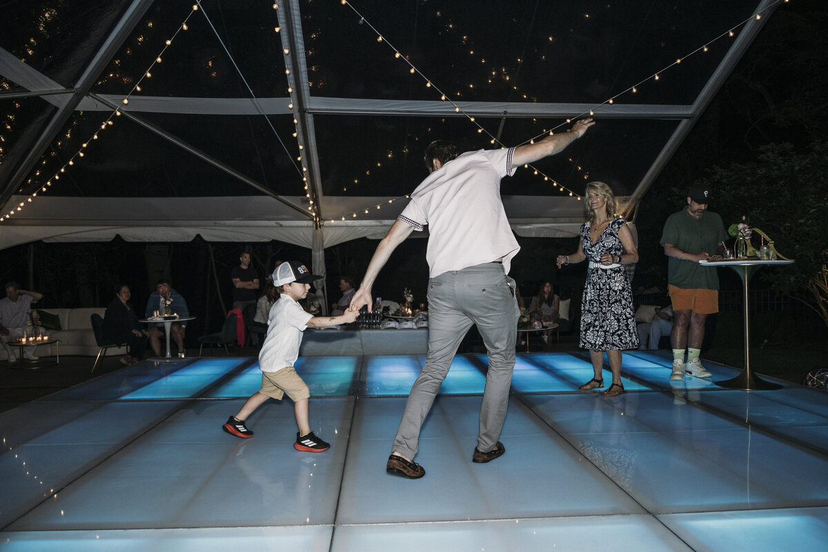 Photo of father and son dancing on neon blue dance floor in private backyard party by Mira Park Photography NY based wedding photographer