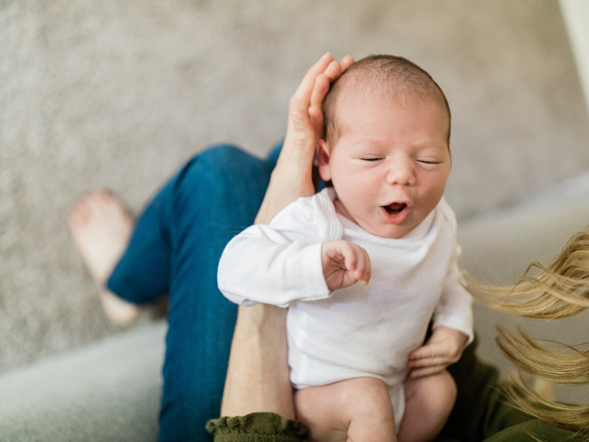 newborn baby boy in white onesie laying in moms lap