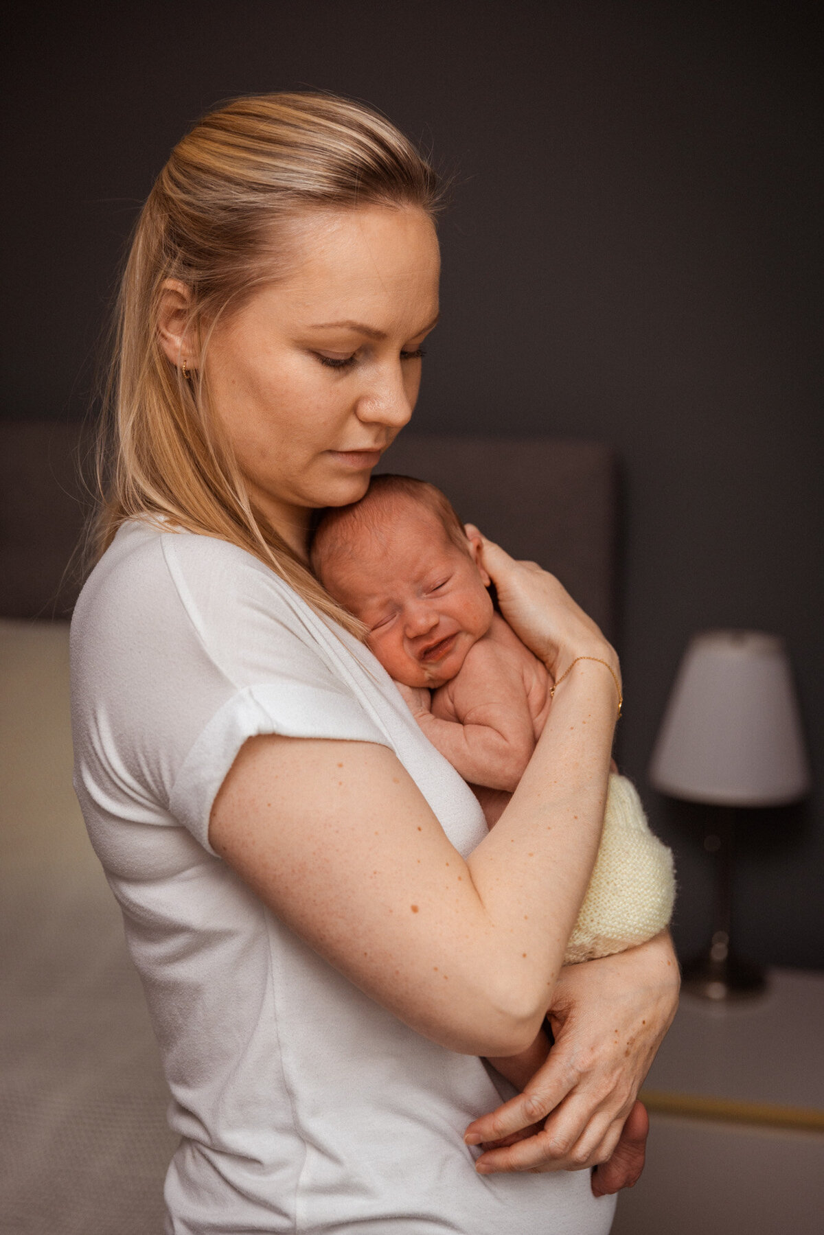 Livsstilsfoto av  en mor i profil, hun holder babyen sin opp til brystkassen sin. Babyens ansikt er vendt mot kamera.