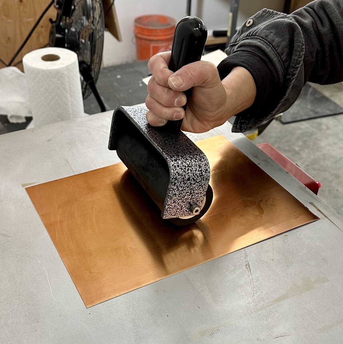Close-up of a person's hand rolling ink onto a copper plate with a brayer for traditional printmaking.